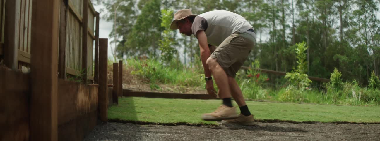 A man is outside laying down sod in his yard