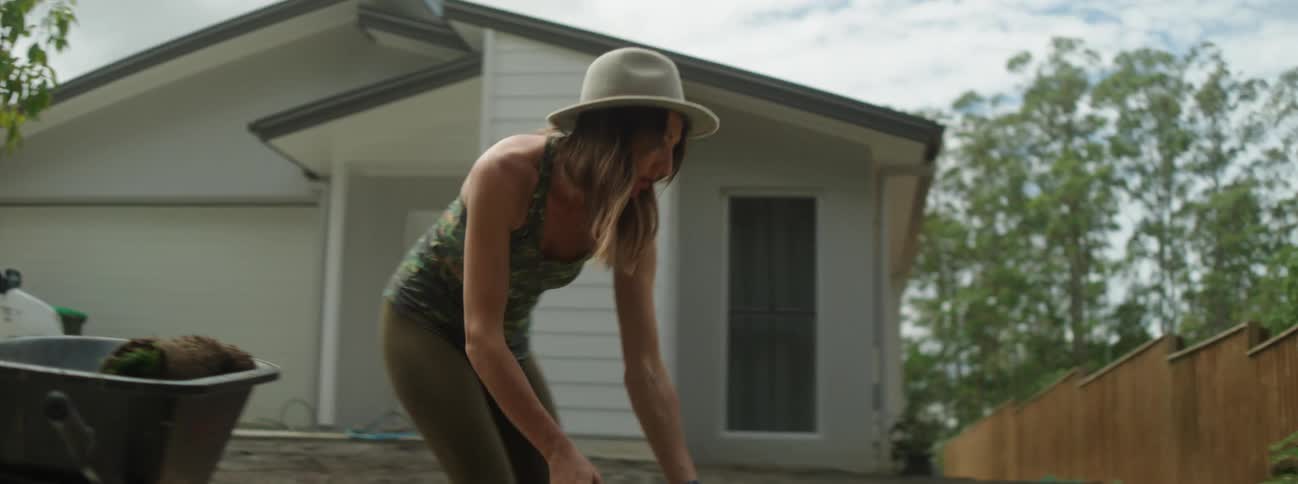 Woman puts strips of sod into wheelbarrow in bare earth yard