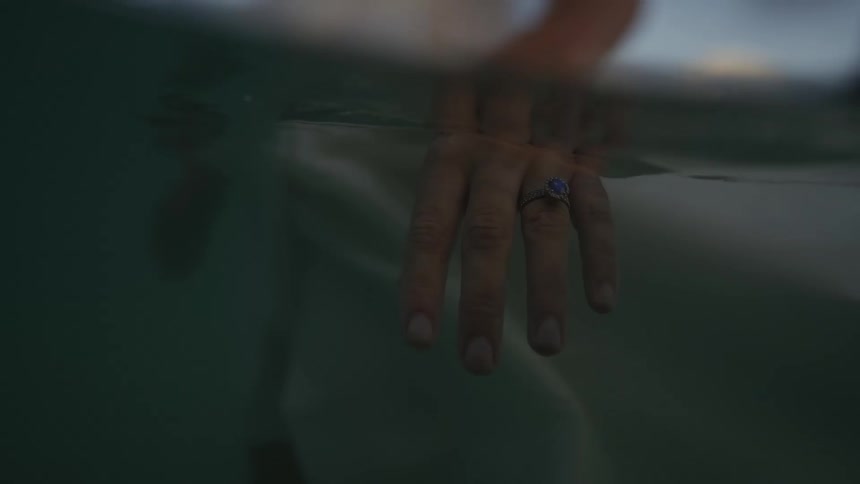 Woman wearing dress stands in water as it bobs up and down over the ring on her finger