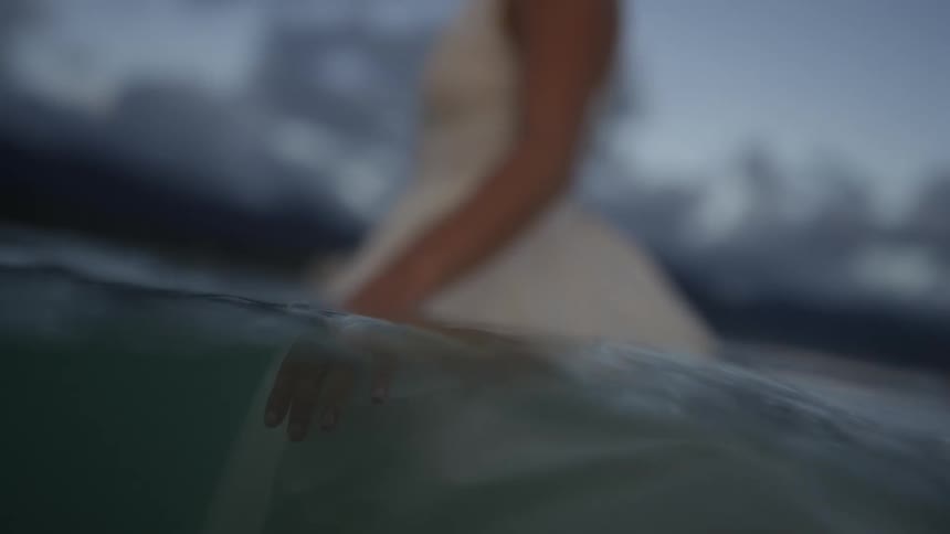 A woman in a white dress is standing in the water at the beach