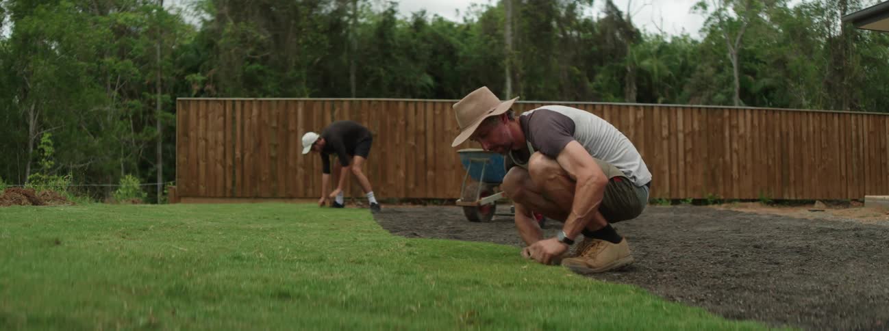 Two men are working outside in a yard laying down sod