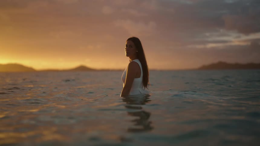Woman in wedding dress stands in water at sunset