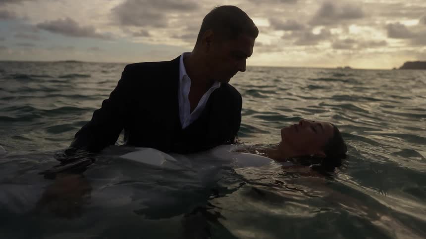 The groom is holding his bride in the ocean