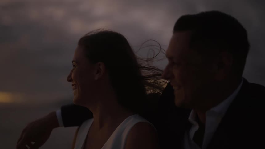 Groom in suit and bride with wedding dress look at sunset laughing