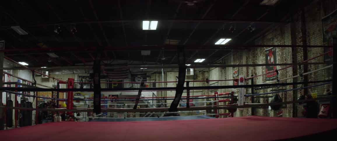The lights come on in a boxing gym and a boxing ring is in the room with punching bags