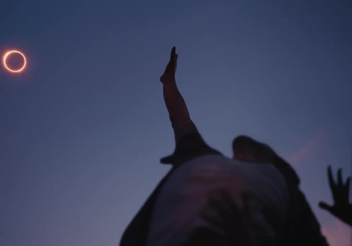 Two people hold their arms up and reach towards a bright ring in the sky