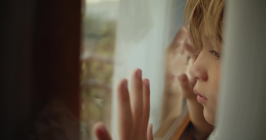 A little boy has his hands pressed on the window and moves his fingers as he looks outside