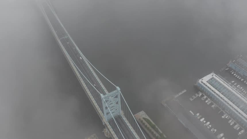 Traffic moving over a suspension bridge is seen through the fog and smoke from above