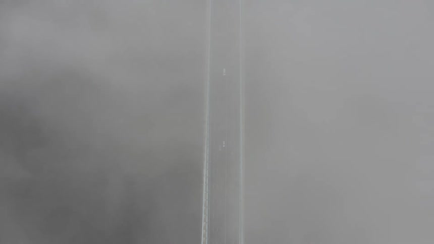 Aerial view of suspension bridge with vehicles crossing seen from clouds