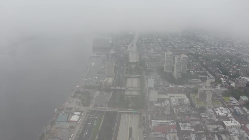 Traffic parallels waterfront while moving along highway through city on a foggy day