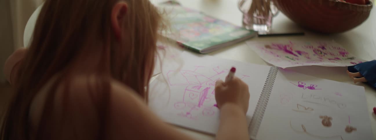 Girl with red hair sits at table drawing in notebook