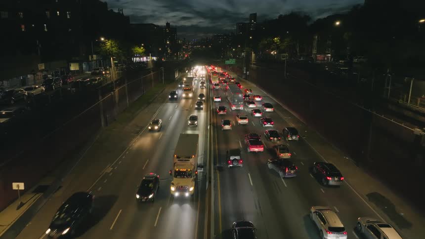 Headlights and tail lights glow in the darkness as traffic moves on a highway through town