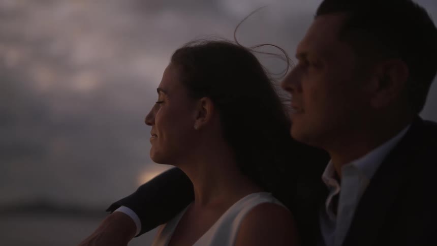 A man rests his arm around a womans neck as they look out at the water
