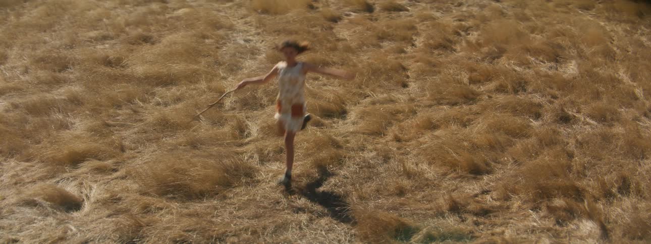 A young woman runs through a field while carrying a stick during the day