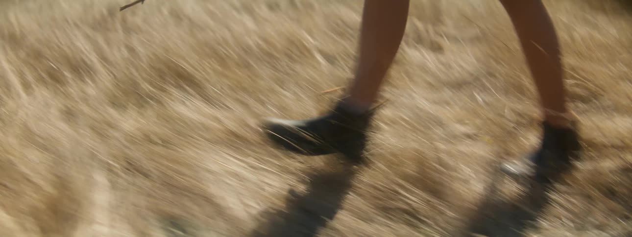 Girl in skirt and a pair of black shoes walks in field with brown grass