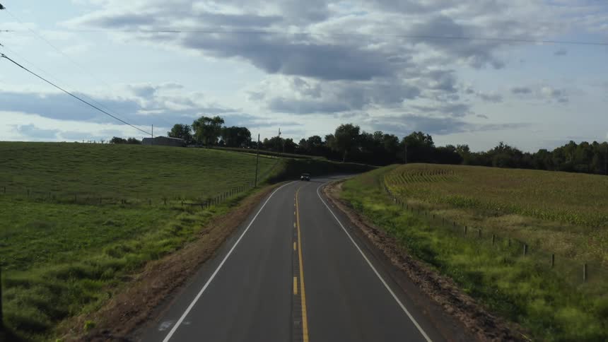 Automobiles travel on a road through rural farmland under a cloudy sky