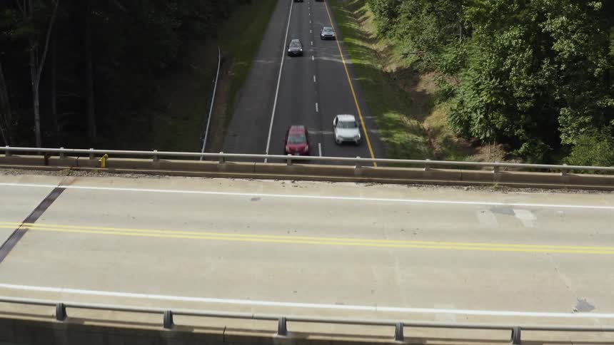 An overhead shot of a bridge going over a two lane highway with cars driving down it