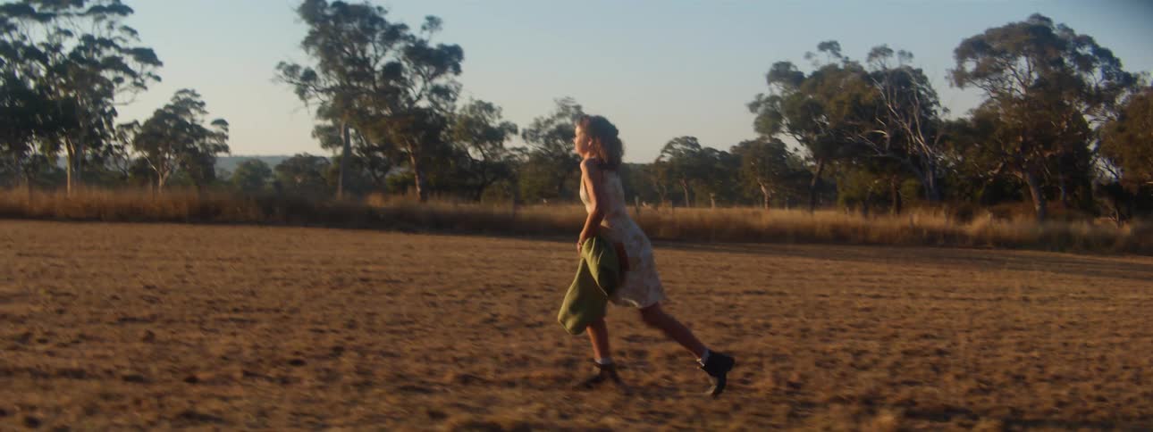 A young girl takes off her jacket and runs across a field