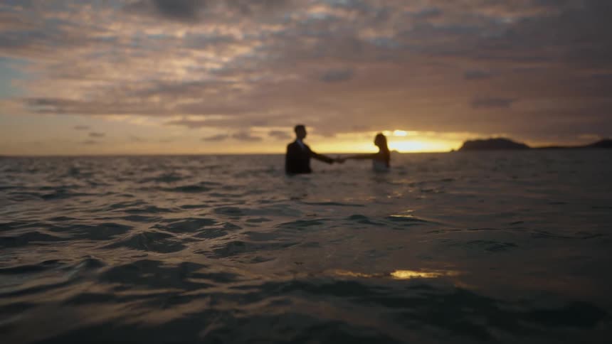 A couple walk towards each other to hold hands in the ocean
