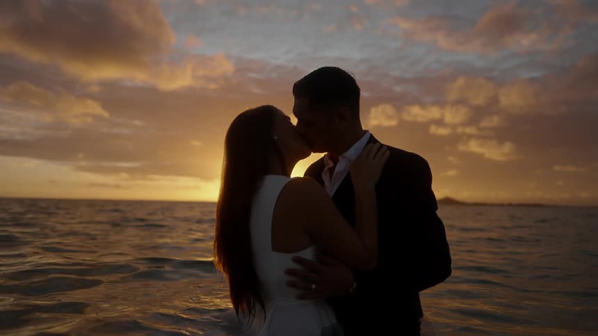 A husband and wife hold each other compassionately and then share a kiss against the sunset