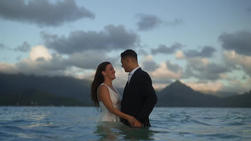 A bride and groom kiss while standing in the ocean