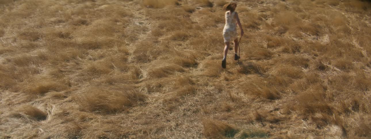 A young woman runs through a field carrying a stick during the day