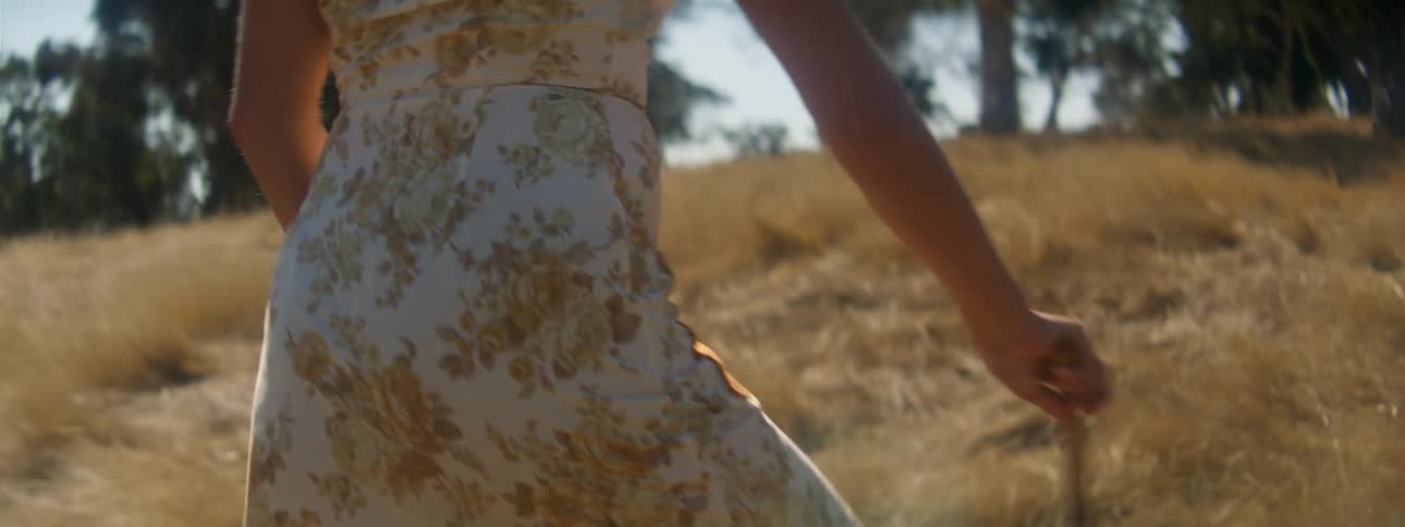 Woman in white floral dress walks in brown grassland area