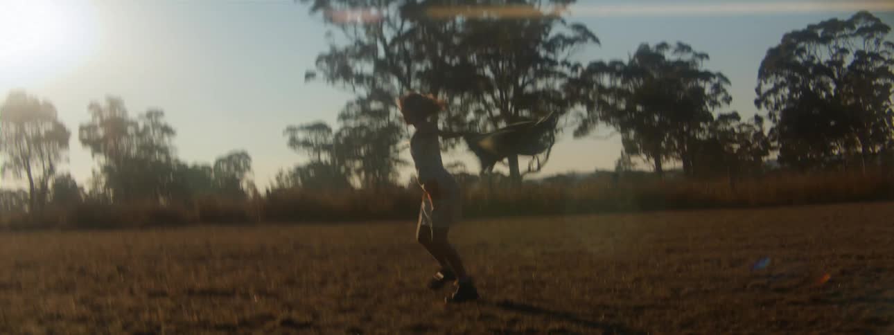 Woman spins and skips while crossing pasture on sunny day