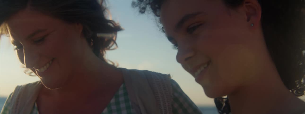 The sun shines brightly upon a woman and her daughter as they walk on the beach