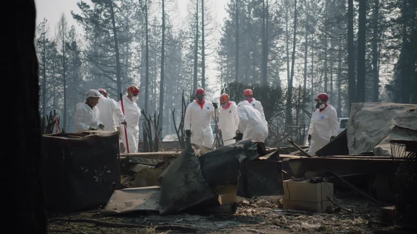A small group of workers in white suits pick through rubble and debris