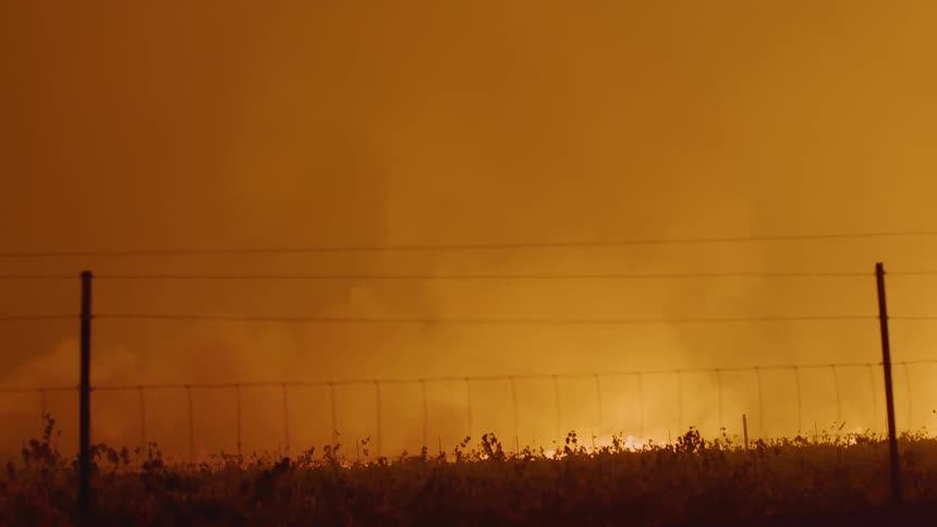 Fire burns on other side of wire fence filling the air with smoke