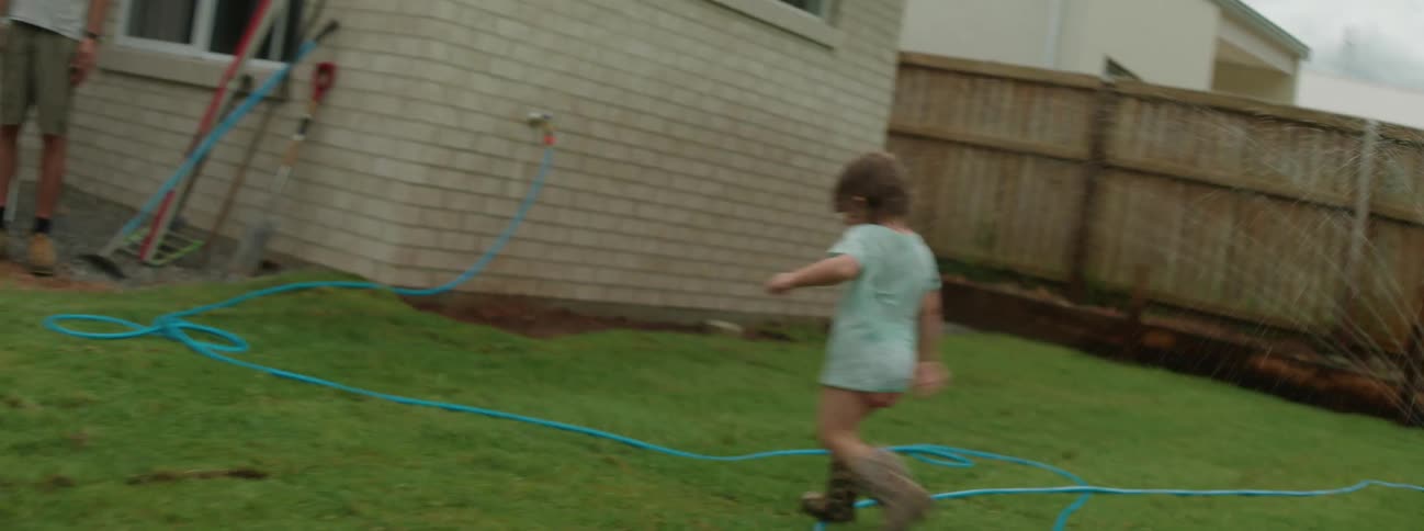 A young child running through a sprinkler in the yard