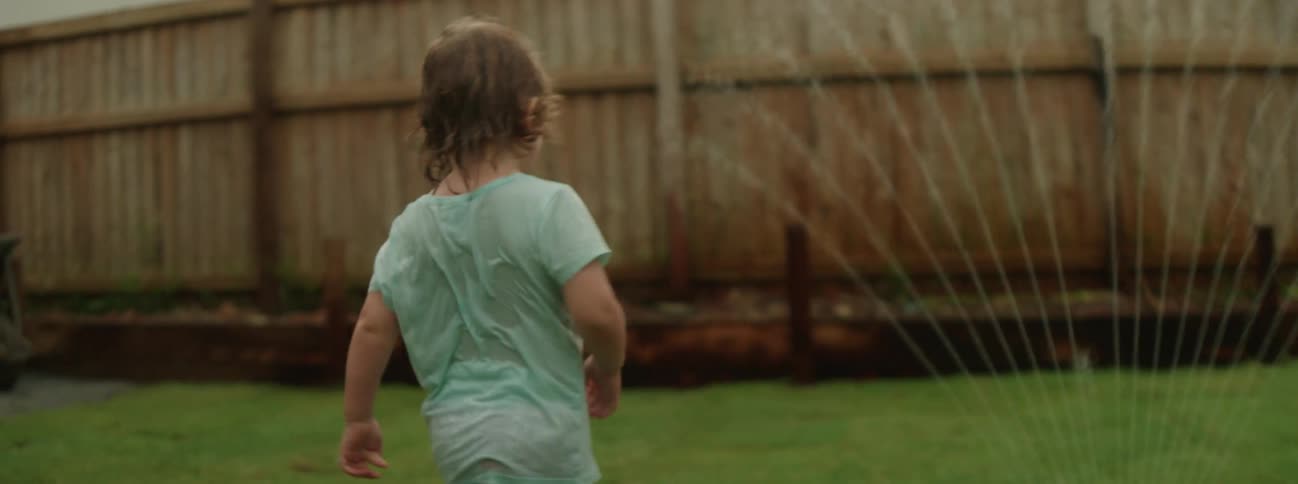 A child running through a sprinkler in a yard