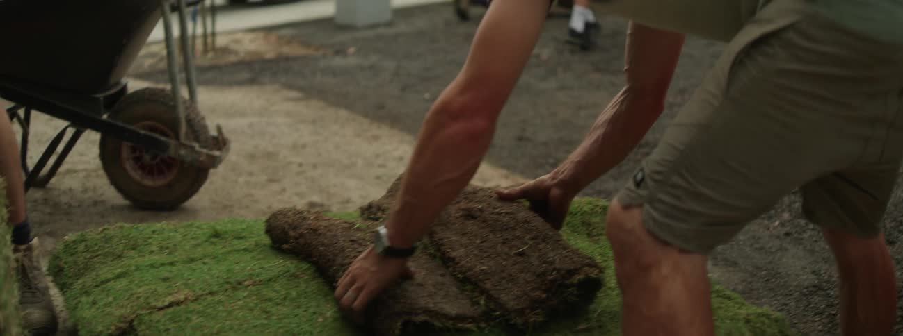 A person folds and picks up grass and walks away with it