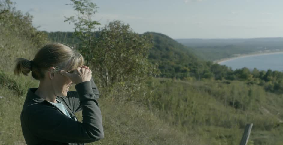 A woman looks out towards the coast while standing at a higher elevation