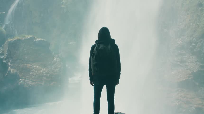 A hiker watches a large waterfall come down the side of a canyon