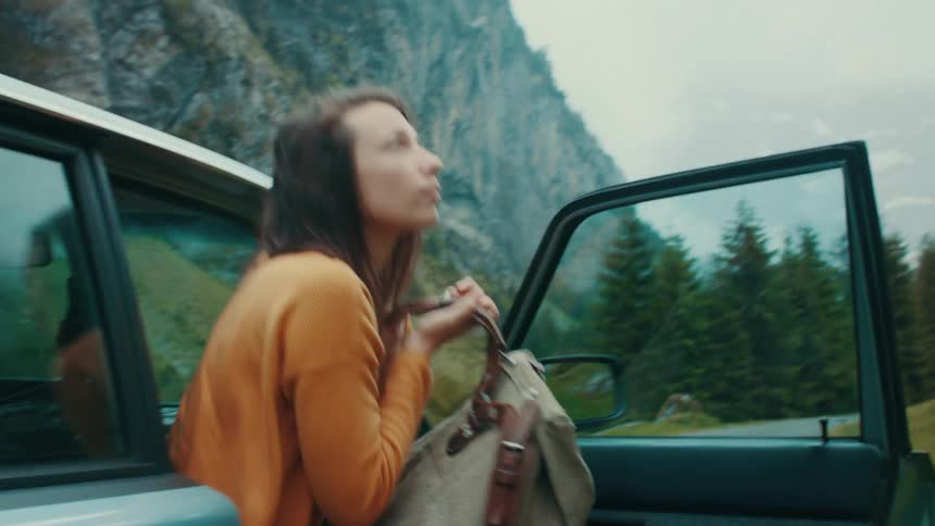 A woman gets out of a car with a camping backpack and begins to walk towards a mountain