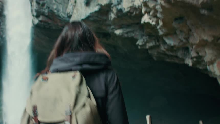 A backpacker hikes past a waterfall and into a cave