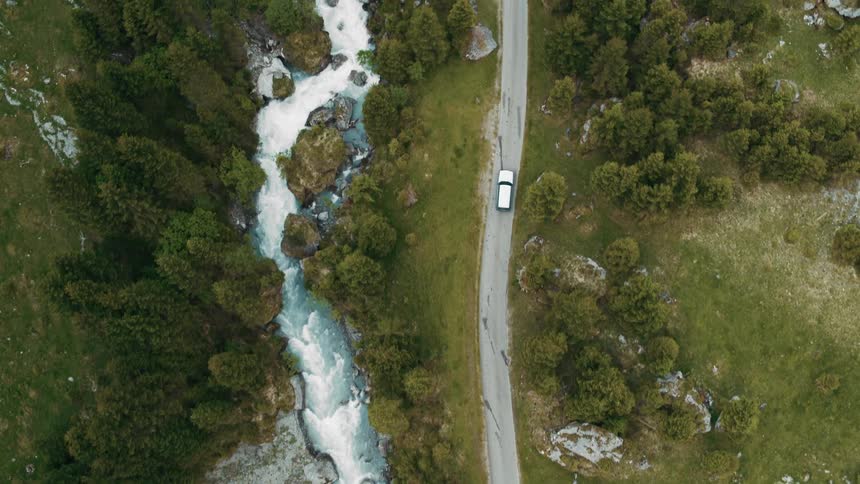 An automobile travels on a road alongside a stream and through woods