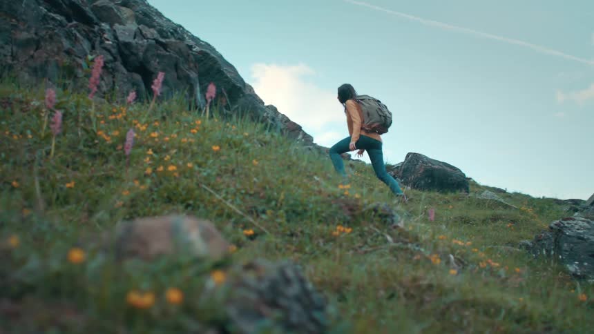 A woman wearing a camping backpack takes larges steps while hiking up a steep mountain