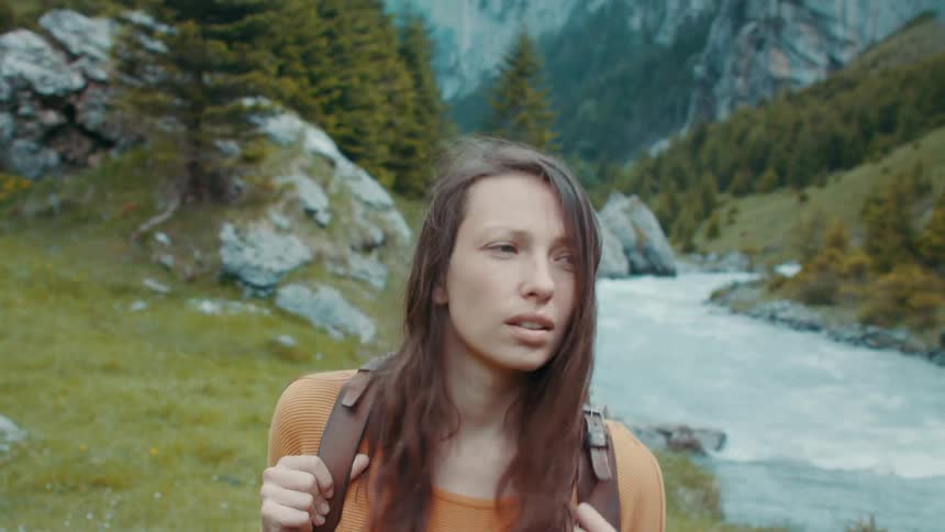A woman hikes along side a rapid river at the base of a mountain range