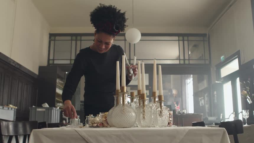 A woman organizes salt shakers as she prepares to set tables at a restaurant