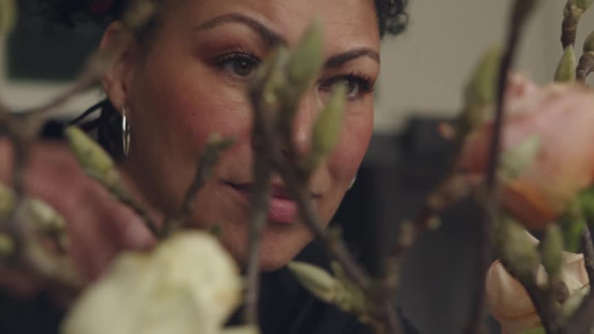 Woman with hoop earrings and black shirt look at pink roses and buds in room