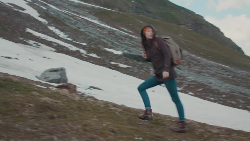 A woman hiker walking up a hill carrying a backpack and her jacket hood up