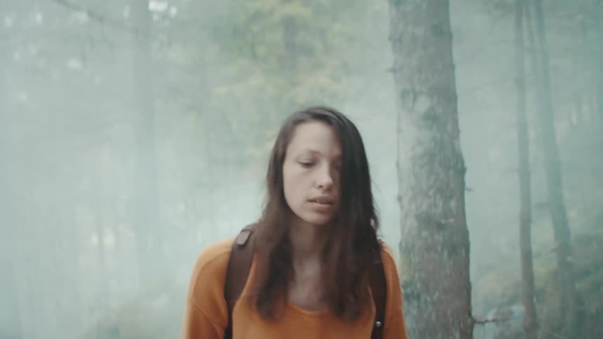 Female backpacker walks through forest on a foggy day