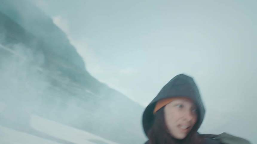 A woman hiking up a snowy mountain struggles and slips on the snow