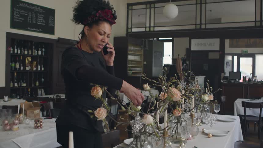 Woman adjusts decorations on table in restaurant while talking on a smartphone