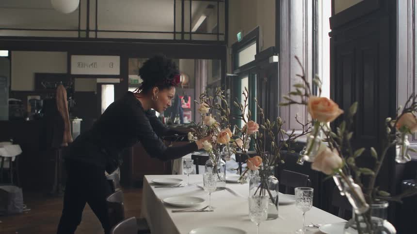 Woman adjusts flower arrangement on dining table in restaurant
