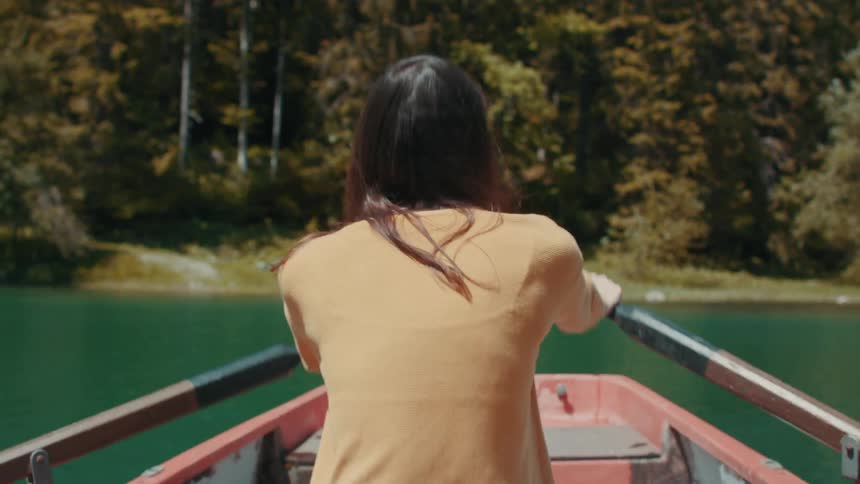 Woman rows boat while facing forest on shore