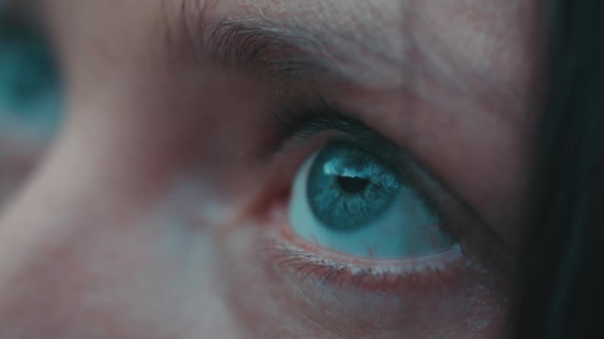 A close up of a womans eye blinks and looks up at something